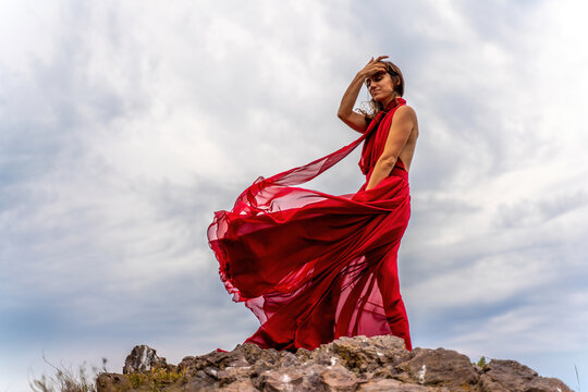 Woman in red dress dance over storm sky, gown fluttering fabric flying as splash