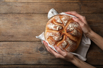 Woman holding loaf of tasty wheat sodawater bread at wooden table, top view. Space for text