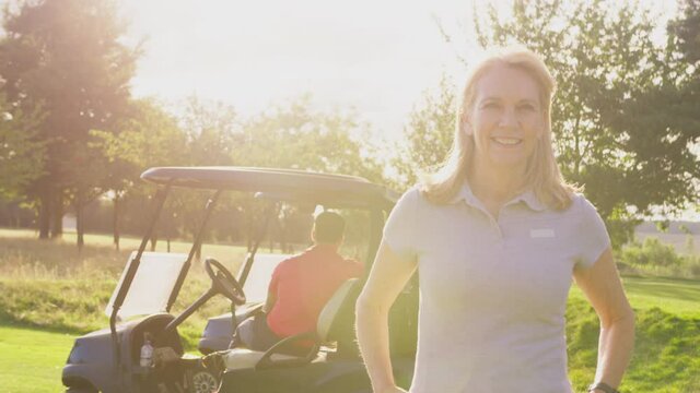 Portrait of smiling mature female golfer standing by buggy with male playing partner on course with lens flare- shot in slow motion