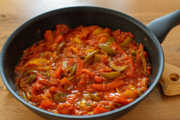 Stewed sweet bell peppers in tomato sauce (or pepperonata) in a skillet on a wooden background.