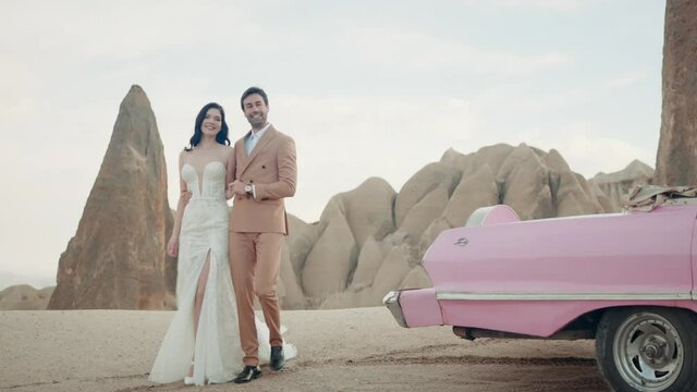 Beautiful young couple during photo session on the top of a mountain in Cappadocia. Action. Romantic love of man and woman couple near the cabriolet pink car.