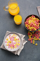 Fototapeta na wymiar Bowls with colorful cereal rings and glass of juice on dark background