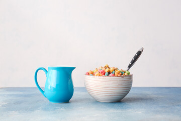 Bowl of colorful cereal rings and jug of milk on color background