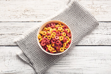 Bowl of colorful cereal rings on light wooden background