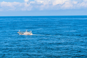 Fishing trawler in ocean water under cloudy blue sky.