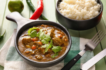 Frying pan with tasty beef curry and rice in bowl on table