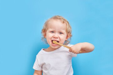 left-handed child brushes his teeth with a bamboo toothbrush on a plain background with a place for...