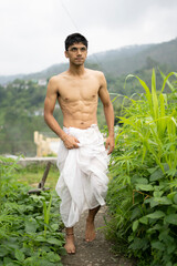 Young Indian fit boy, walking on a pathway beside crops in the field. An Indian priest walking...