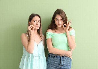 Young gossiping women on color background