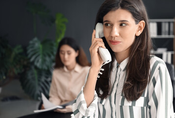 Young woman gossiping while talking by phone in office