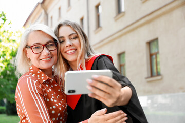 Happy young woman with her mother taking selfie on graduation day