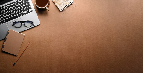 Computer laptop, glasses, coffee cup and notepad on brown background. Top view.