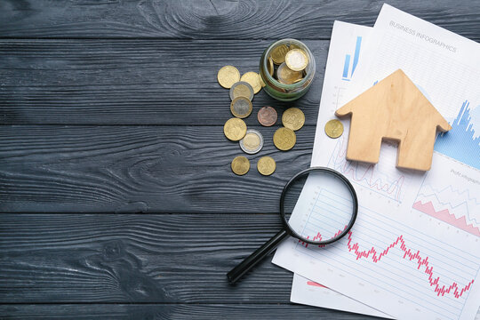 Wooden house with magnifier, diagrams and coins on dark wooden background