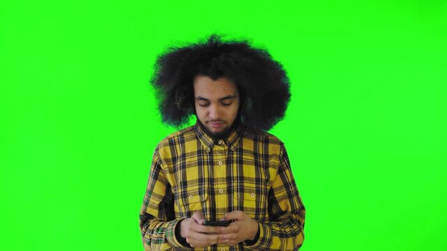 A young man with an African hairstyle on a green background is talking into his phone.