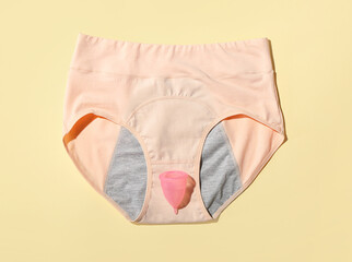 Period panties and menstrual cup on color background