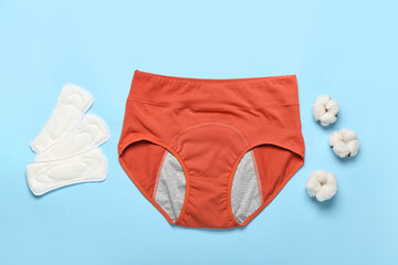 Period panties, pads and cotton flowers on color background