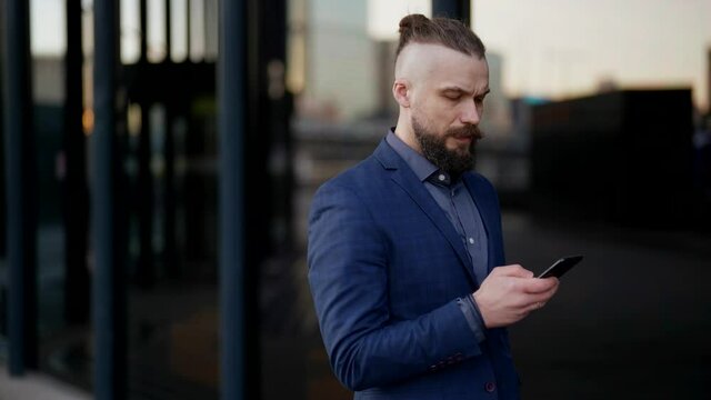confident and successful businessman is surfing internet by smartphone on street