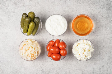 A variety of fermented foods for gut health. Bowls on a gray background. Cucumbers, tomatoes, sauerkraut, yogurt, cottage cheese, apple cider vinegar.