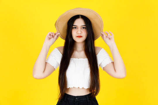 Portrait studio shot of Asian young beautiful sexy long black hair female model wearing crop top outfit dental care braces standing smiling holding hand touching adjusting hat on yellow background