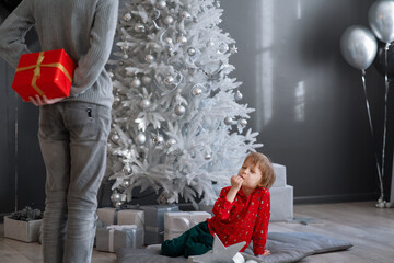 Elder brother giving gift to younger sibling in festive decorated living room with Christmas tree. Gifts and gift giving