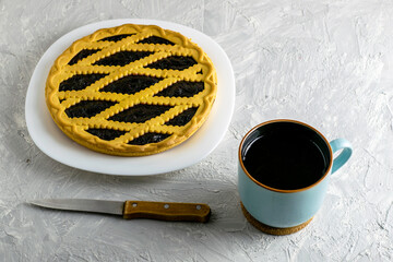 a shortbread pie with blueberries on a white plate with a cut piece, a knife and a mug of tea on the table