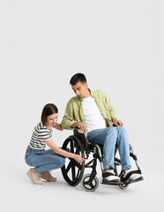 Fototapeta na wymiar Young woman and her husband having problem with wheelchair on light background