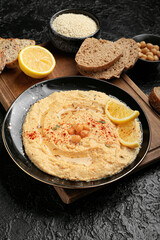 Plate with delicious hummus, bread and lemon on dark background