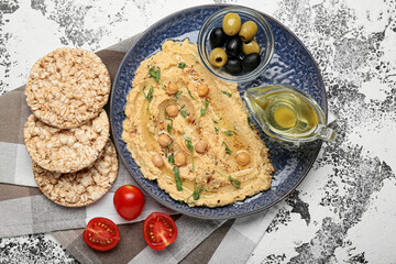 Plate with delicious hummus, rice crackers, olives and oil on grunge background