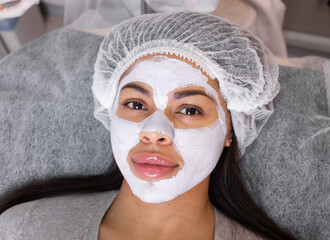 Cosmetology. Cosmetologist applies a cleansing mask on black woman face with a brush. Cosmetic procedure for facial rejuvenation.