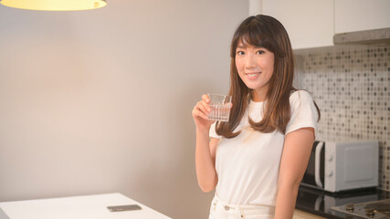 Portrait of young beautiful woman drinking glass of water in kitchen