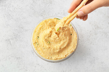 Woman eating delicious hummus on light background