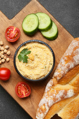 Bowl with delicious hummus, bread and vegetables on dark background
