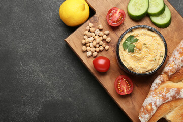 Bowl with delicious hummus, bread and vegetables on dark background