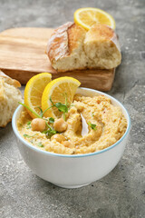 Bowl with delicious hummus and lemon on grey background, closeup