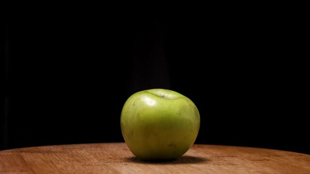 A green apple on a wooden board on a black background. The camera flies around. Parallax effect. An apple of the renet simirenko variety