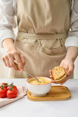 Woman making delicious sandwich with hummus at table