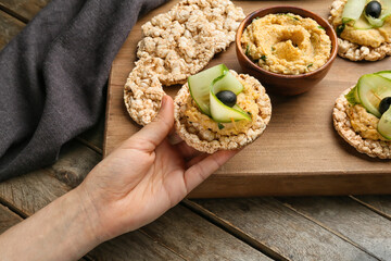 Woman holding rice cracker with delicious hummus on wooden background
