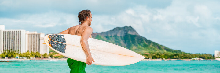 Surfer man going surfing on Waikiki beach in ocean waves carrying surfboard. Summer fun watersport...
