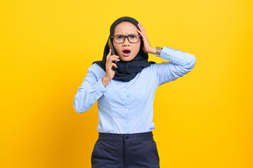 Portrait of surprised young Asian woman talking on mobile phone with open mouth, reaction awesome news isolated on yellow background
