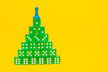 A group of green cubes lies in the form of a pyramid or stacks in ascending order on a yellow background of the text space: a Christmas tree made of green game cubes with a playing chip on top