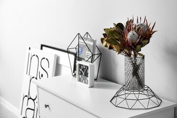 Vase with flowers, magazine and clock on shelf near light wall