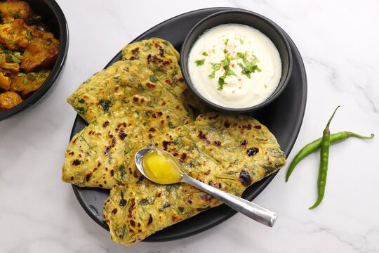 A Food called Methi paratha or Methi thepla is an Indian breakfast dish served with curd and a spoon full of desi ghee. with copy space. Indian fenugreek flatbread. Healthy lunch or dinner.