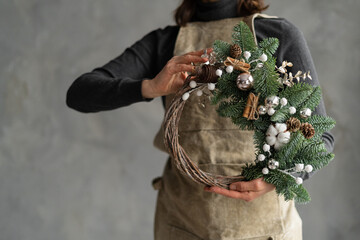 florist hands holding modern christmas wreath, gray wall background. Merry Christmas and Happy...