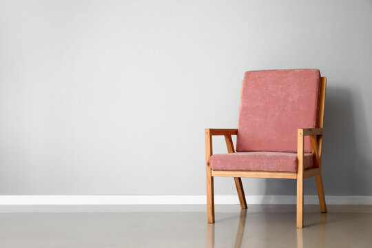 Pink wooden armchair near light wall