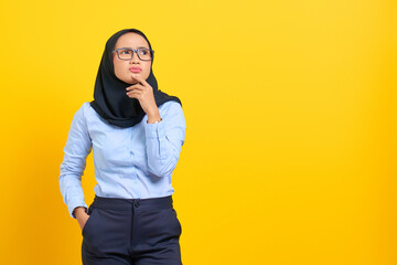 Portrait of pensive young Asian woman looking seriously thinking about a question isolated on yellow background