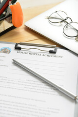 House rental agreement with pen, laptop and eyeglasses on table in office, closeup