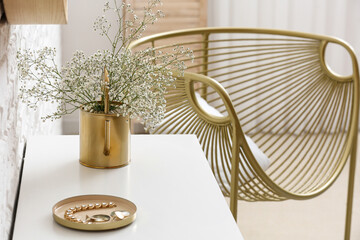 Watering can with beautiful gypsophila flowers and jewelry on table in room