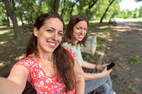 Girlfriends taking selfie together having fun outdoors holding phone looking at camera directly female best friends happy girls travel having great time together friendship spending time