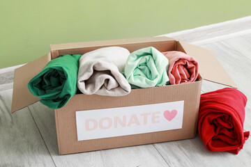 Cardboard box with donation clothes near green wall