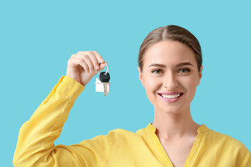 Young woman with key from house on blue background